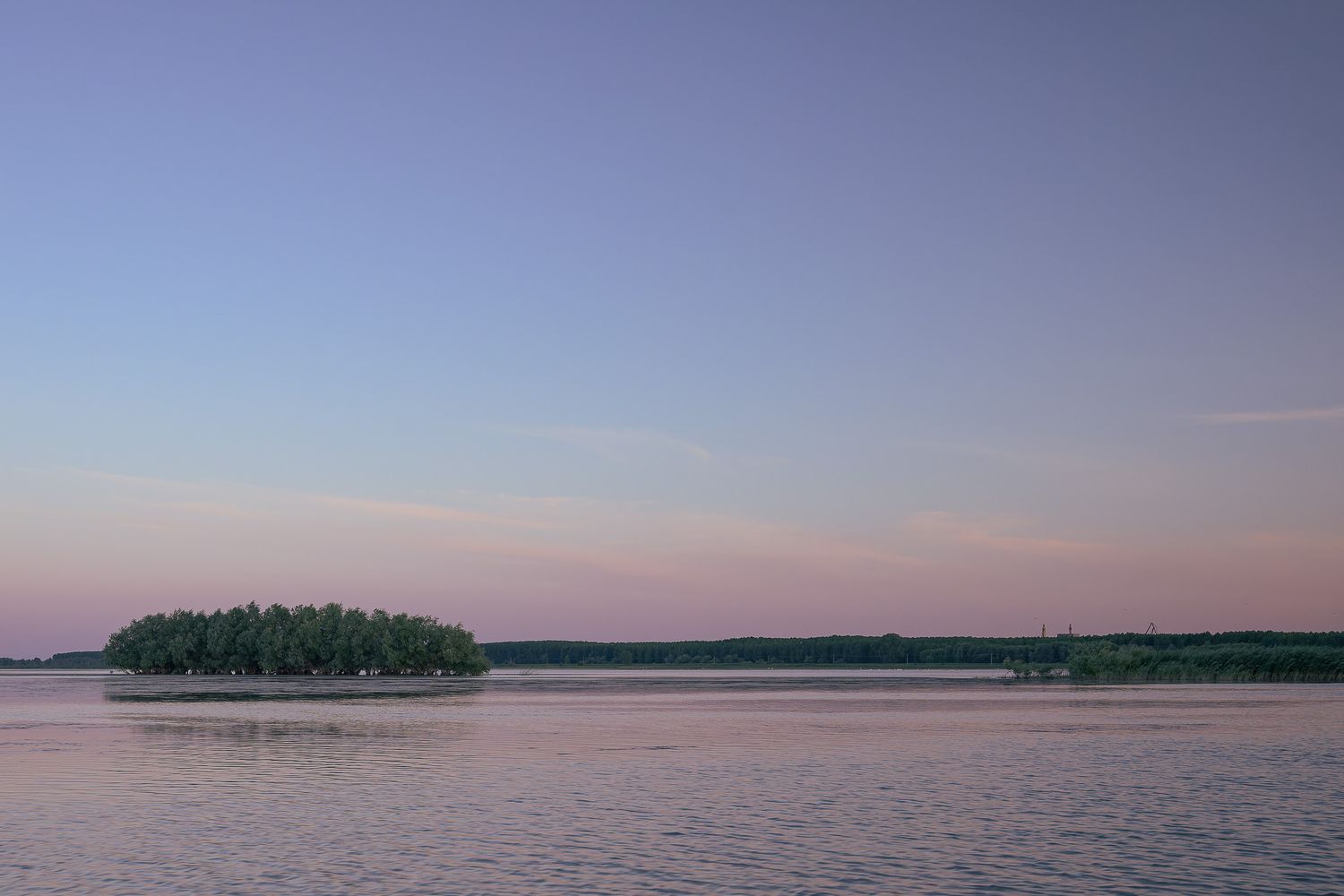 Tranquil sunset view of a small forested island in a calm lake with pink and purple sky at dusk.