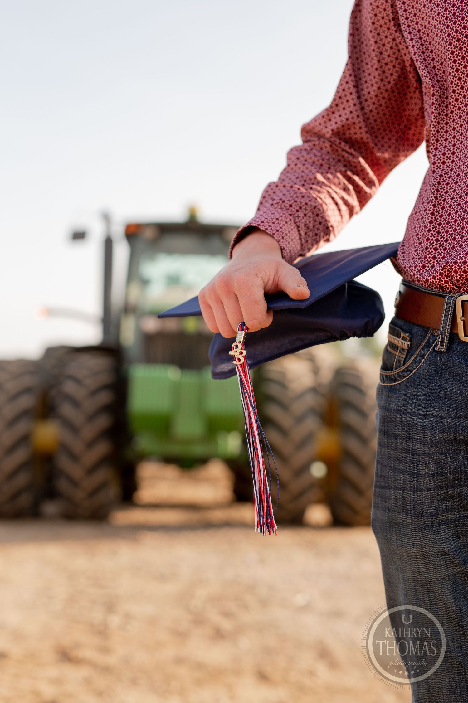Close-up of graduation cap and tassel held against tractor background.