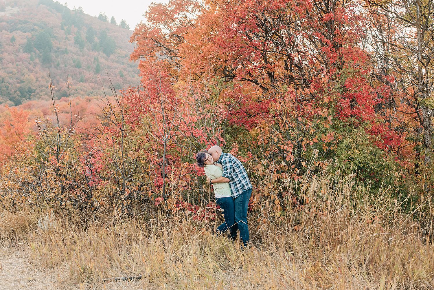 Couple embraces among vibrant red fall foliage on hillside during autumn.