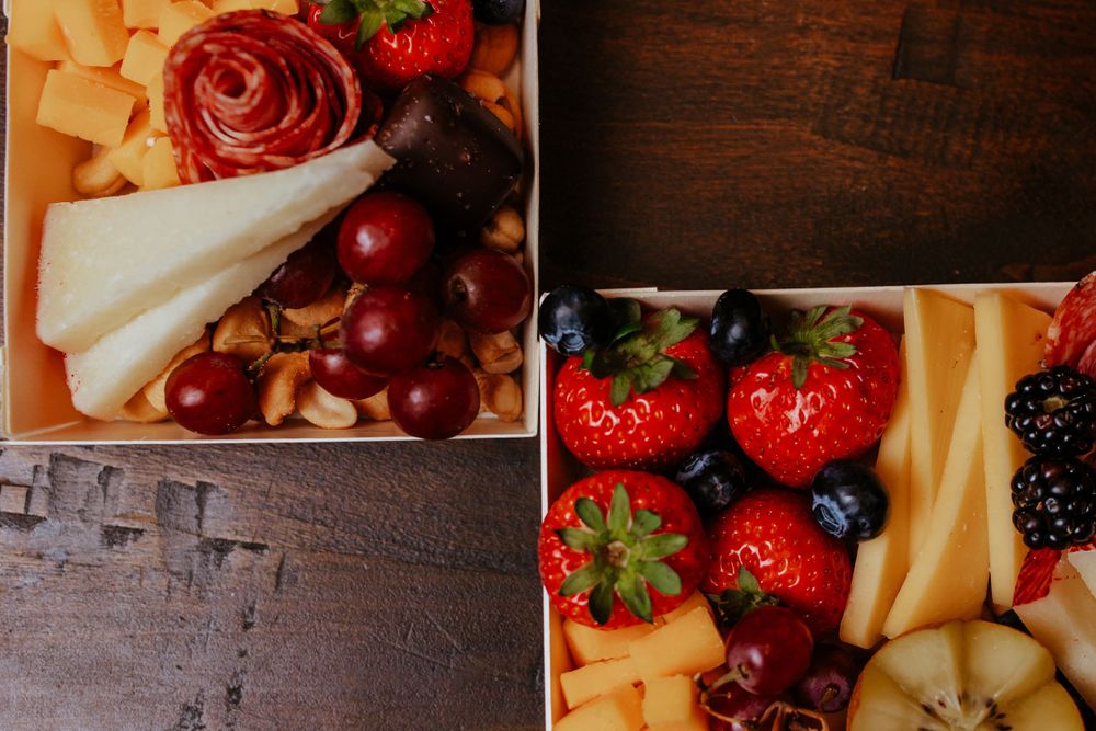 Fresh fruit and cheese platters featuring strawberries, grapes, and cheese slices on wooden surface.