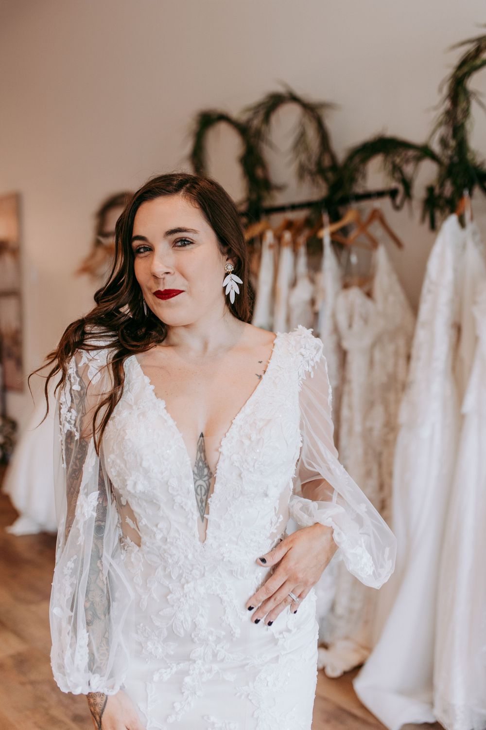 A bride wearing a delicate lace wedding dress with sheer puff sleeves poses in a bridal boutique.