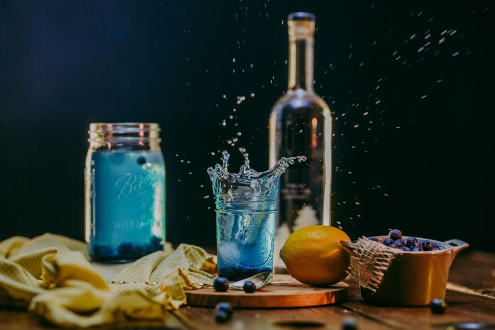 Blue splash cocktail photography with mason jar and citrus on dark background.