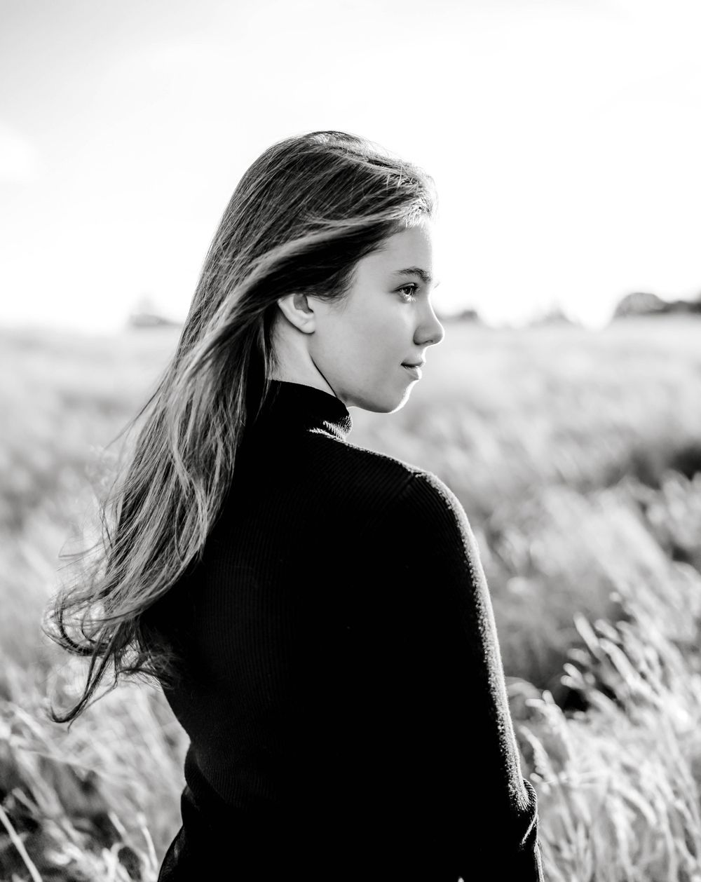 Black and white portrait of teenage girl in field looking away.