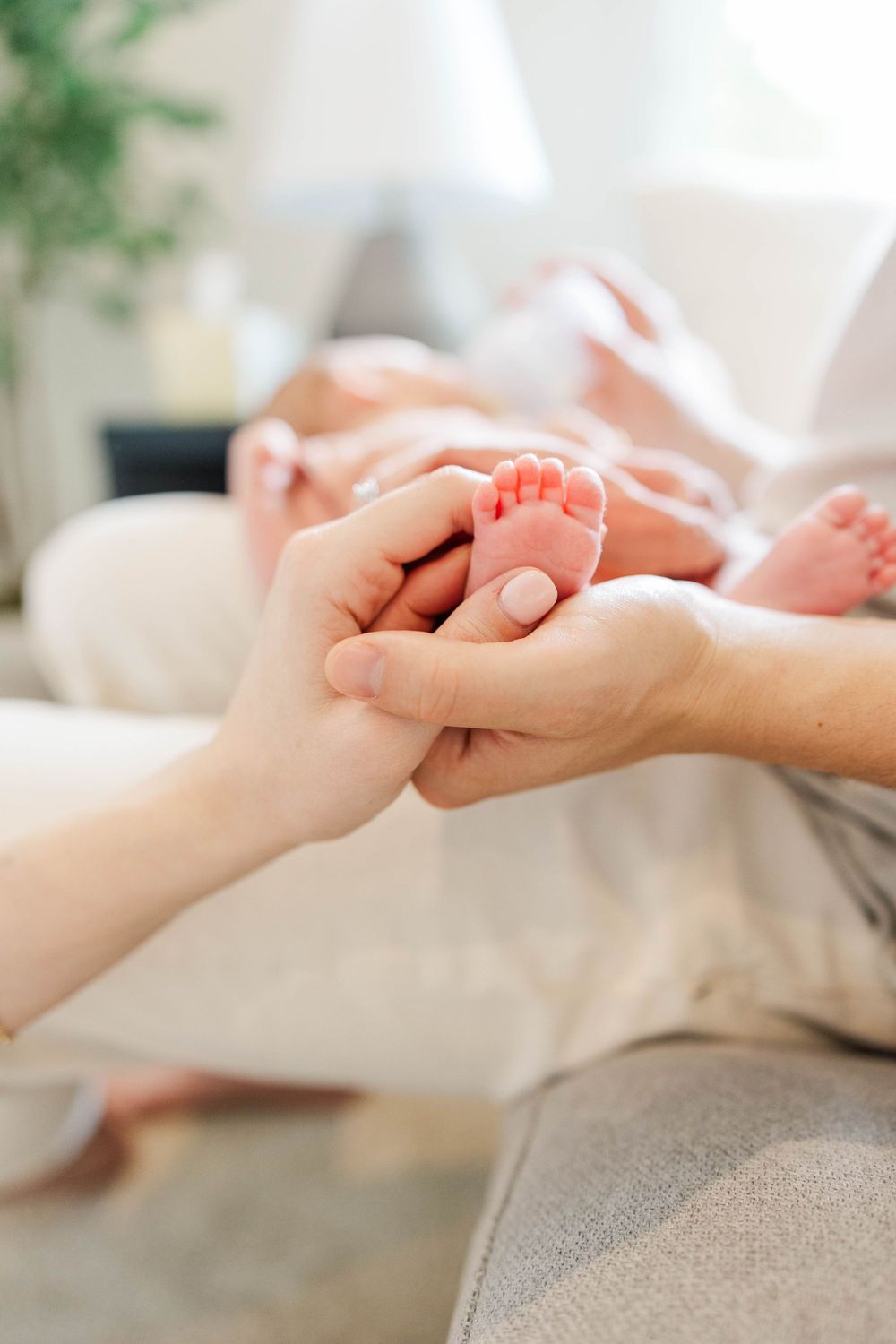 Parents gently holding tiny newborn baby feet in soft natural light indoors.
