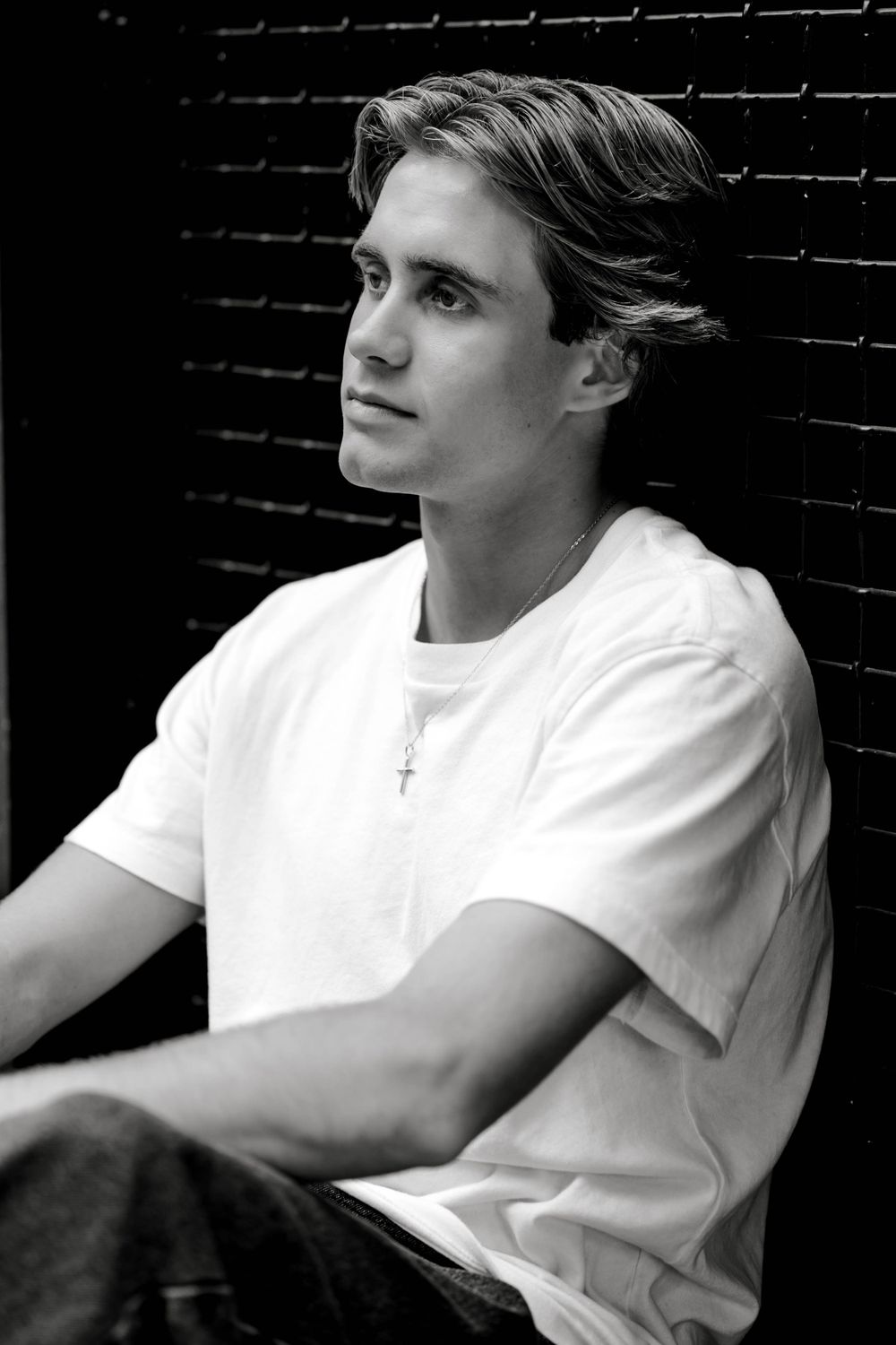Black and white portrait of a teen boy in a white t-shirt against brick.