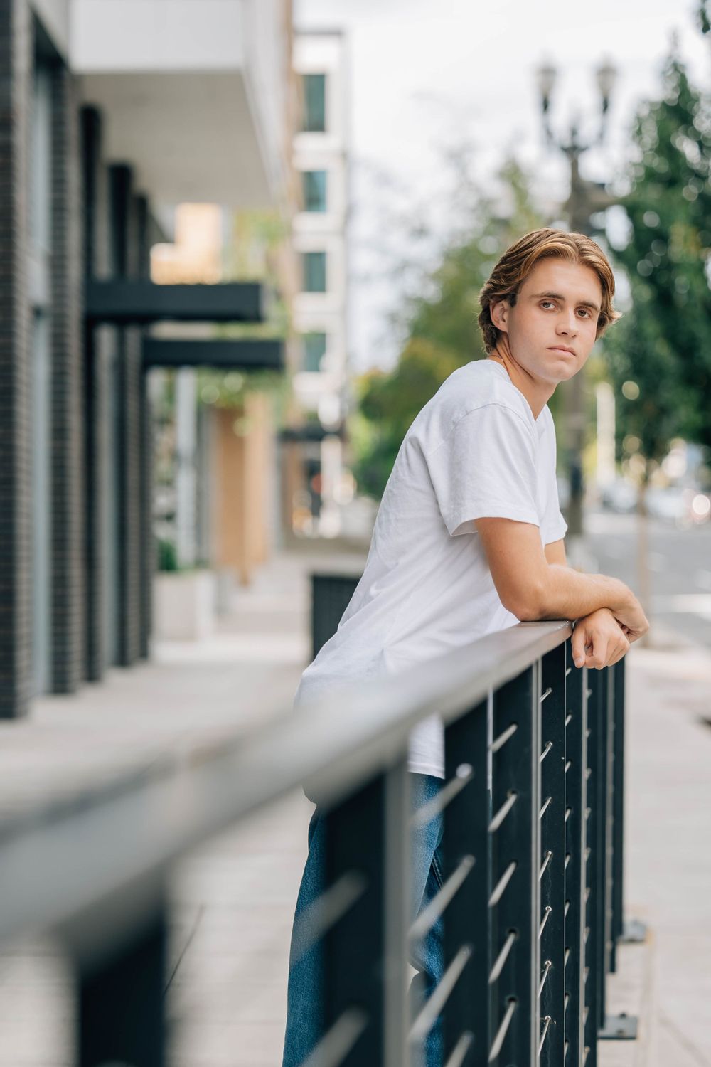 Young man in white t-shirt leaning on urban metal railing outdoors.