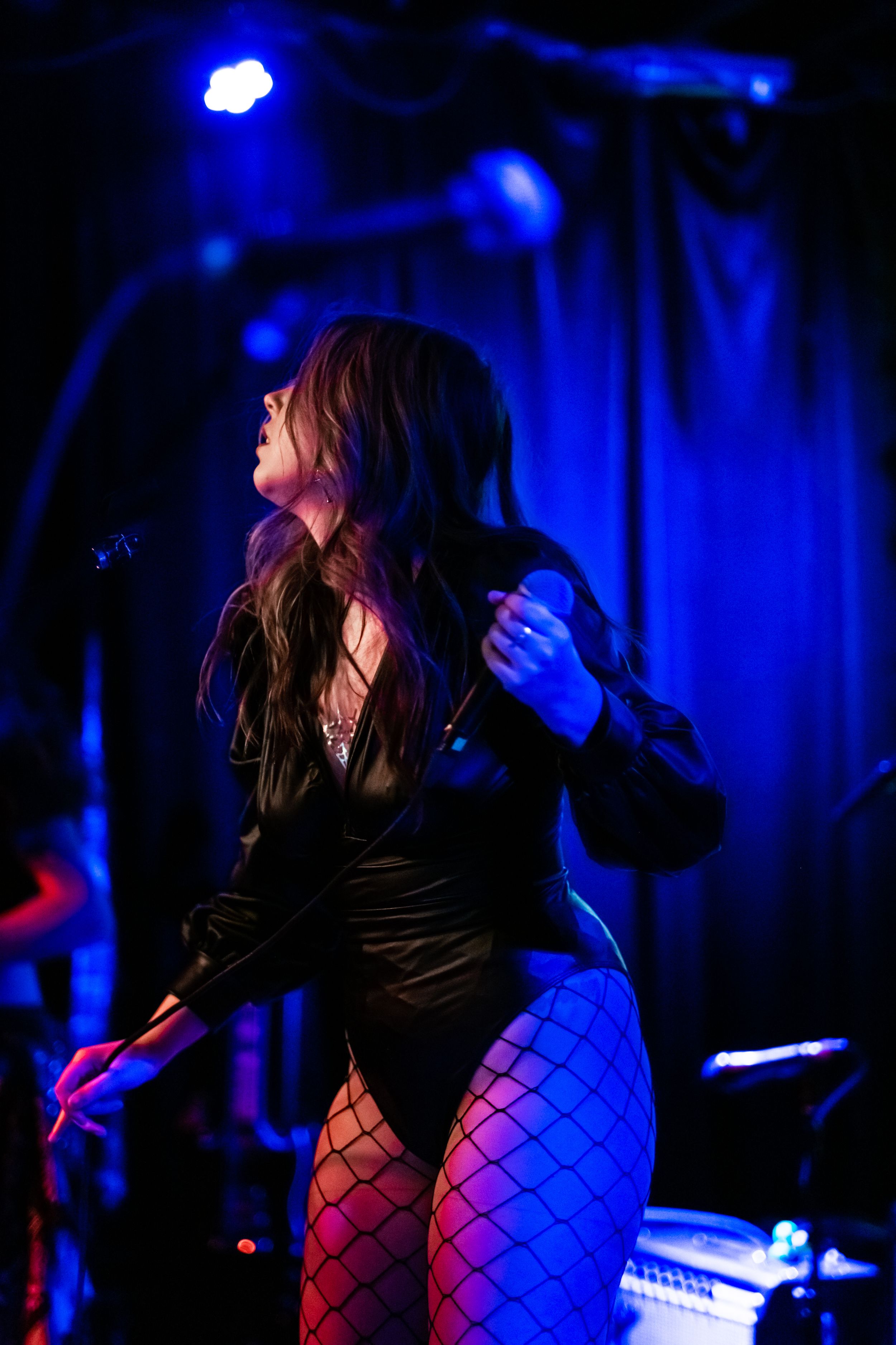 Singer in black outfit performs energetically under blue stage lighting.