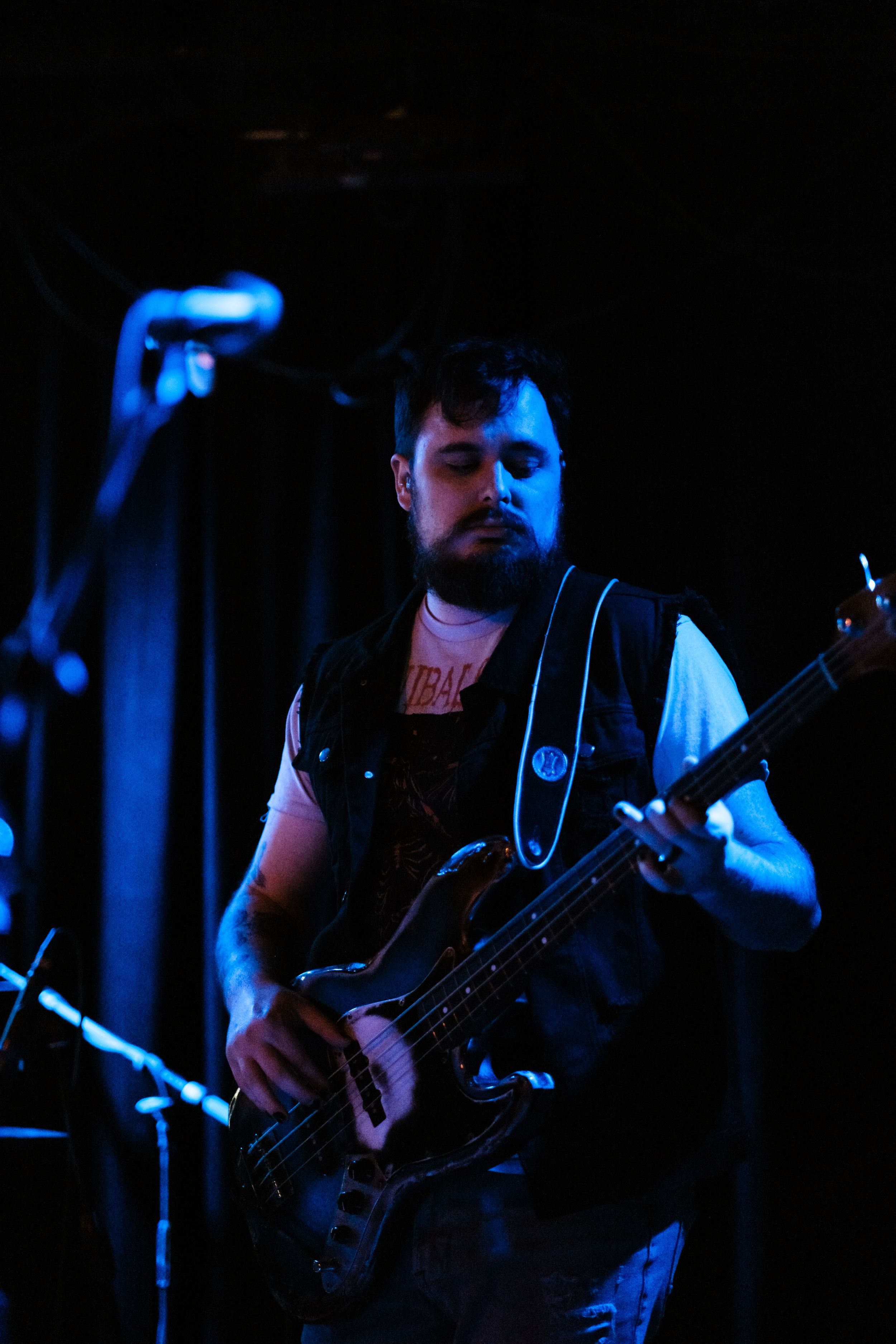Bass player performs on dimly lit stage with blue lighting effects.