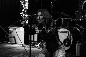 A dynamic black and white performance shot of a singer on stage with a drum kit visible behind.