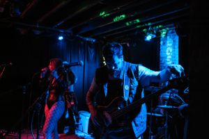 Musicians perform under blue and green stage lighting in a dark venue.