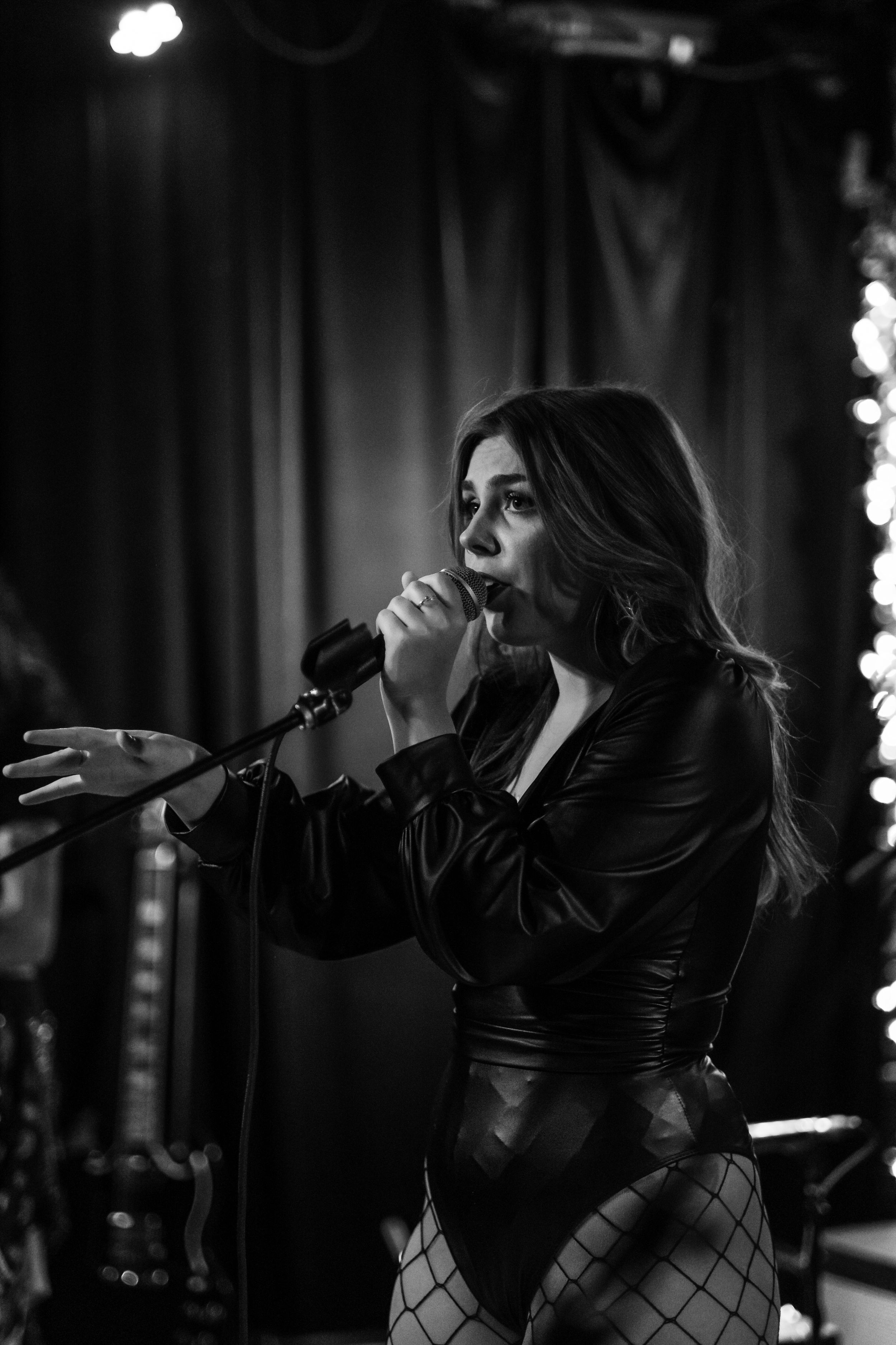 Singer performs passionately on dark stage in leather outfit with dramatic lighting.