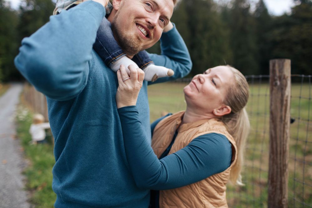 a closeup photo of a mother and father facing each other. There is a baby on the dad's shoulders.