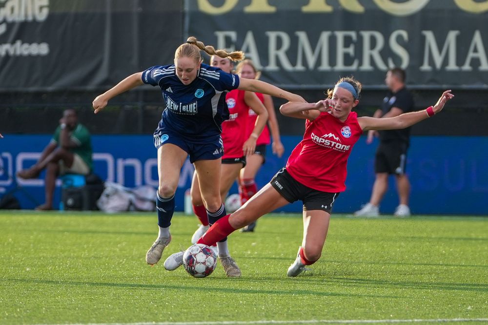 Two soccer players compete for control of the ball during an intense match on a grass field.
