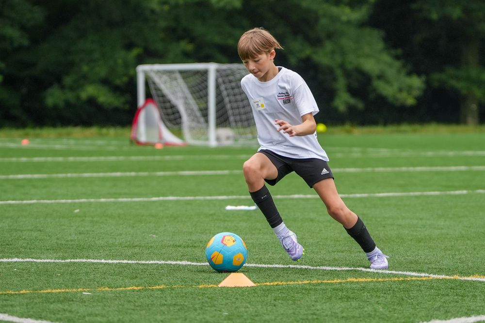 A soccer player in white uniform dribbles the ball across a green grass field during a match.