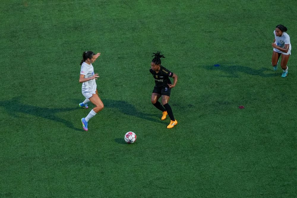Soccer players compete for possession of the ball on a bright green grass playing field during a match.