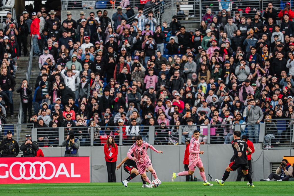 Rugby players compete for possession during an intense match as spectators watch from packed stadium stands.