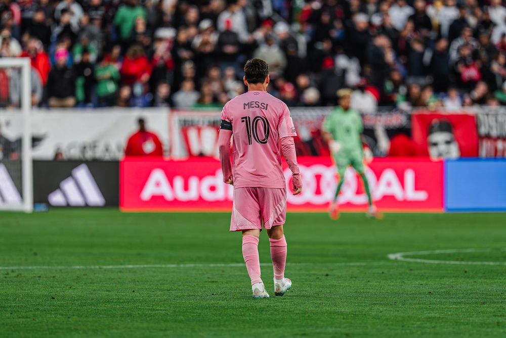 Soccer player wearing pink jersey number 10 stands alone on field with Audi advertisement board visible in background.
