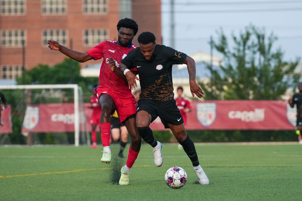 Soccer players from opposing teams compete for control of the ball during an intense match on artificial turf.