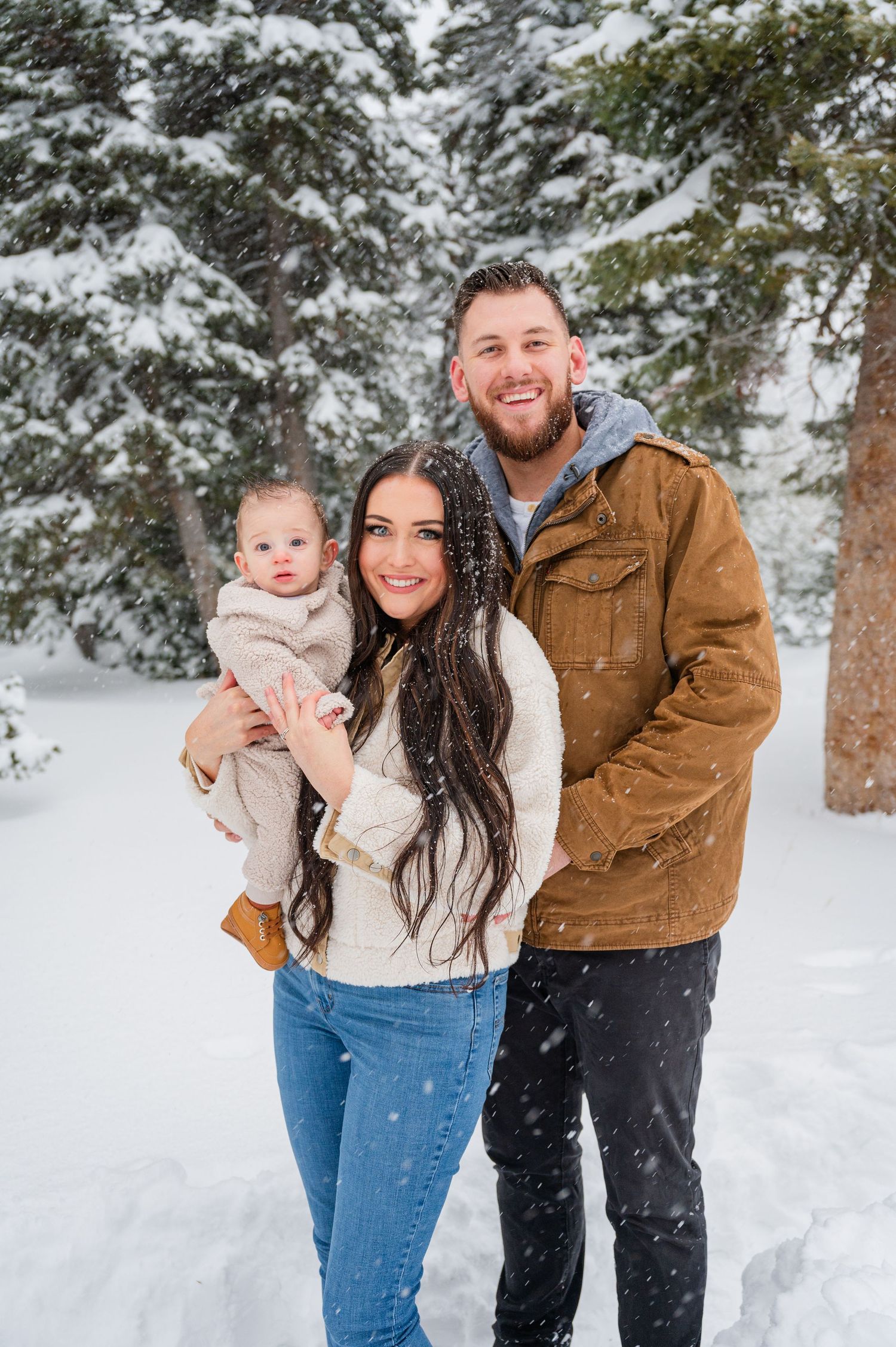 Family portrait in snowy forest with evergreen trees in background.