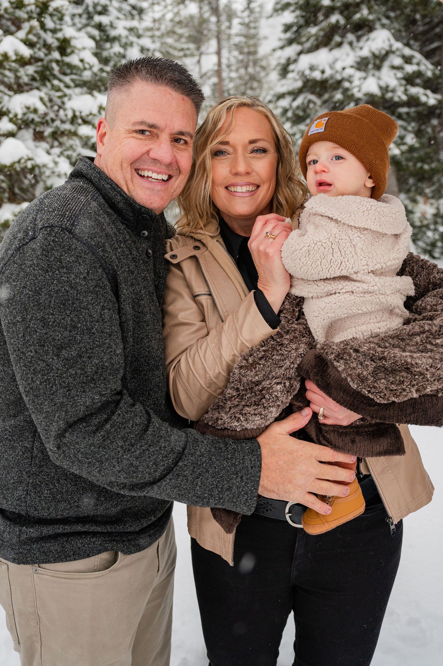 Winter family portrait with snow covered pine trees in the background.