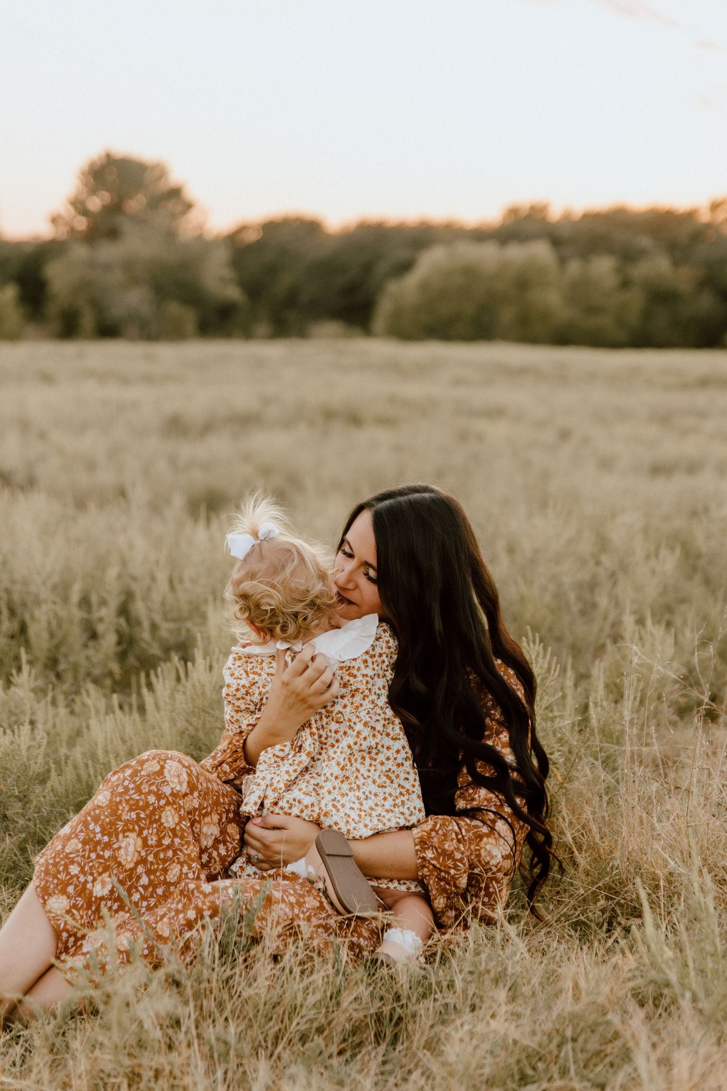 Mother and child in floral dresses sharing sweet moment in golden sunset field. Oklahoma Wedding Photographer