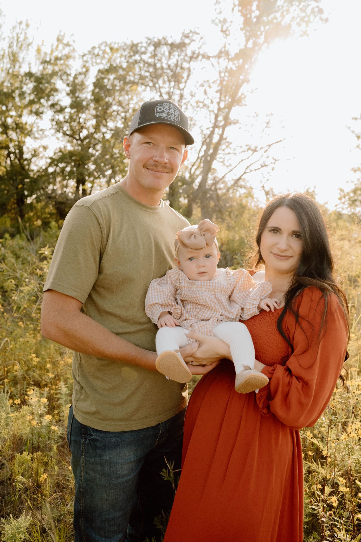 Family of three poses together in a sunlit field during autumn photoshoot. Oklahoma Wedding Photographer