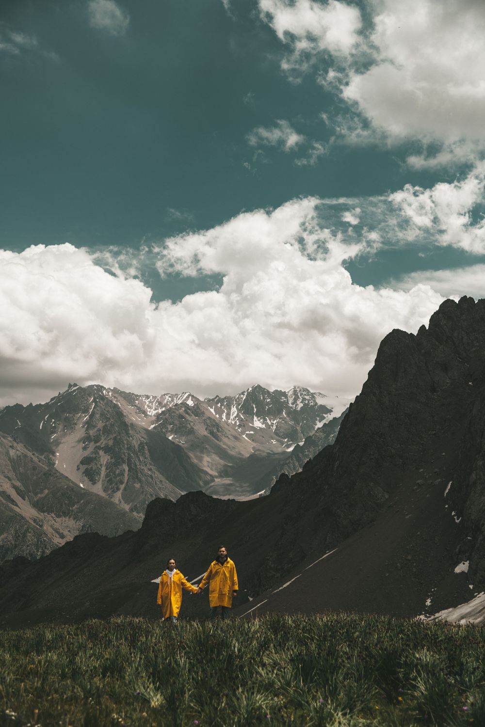 A couple wearing matching bright yellow raincoats, running in the mountains