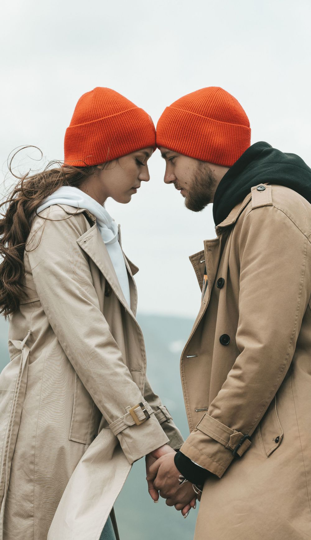 A man and a woman wearing red hats, standing forehead to forehead and holding hands