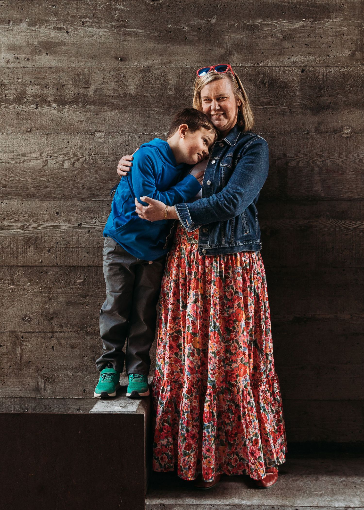 Intimate portrait against concrete wall showing connection between two people in casual denim and floral dress.