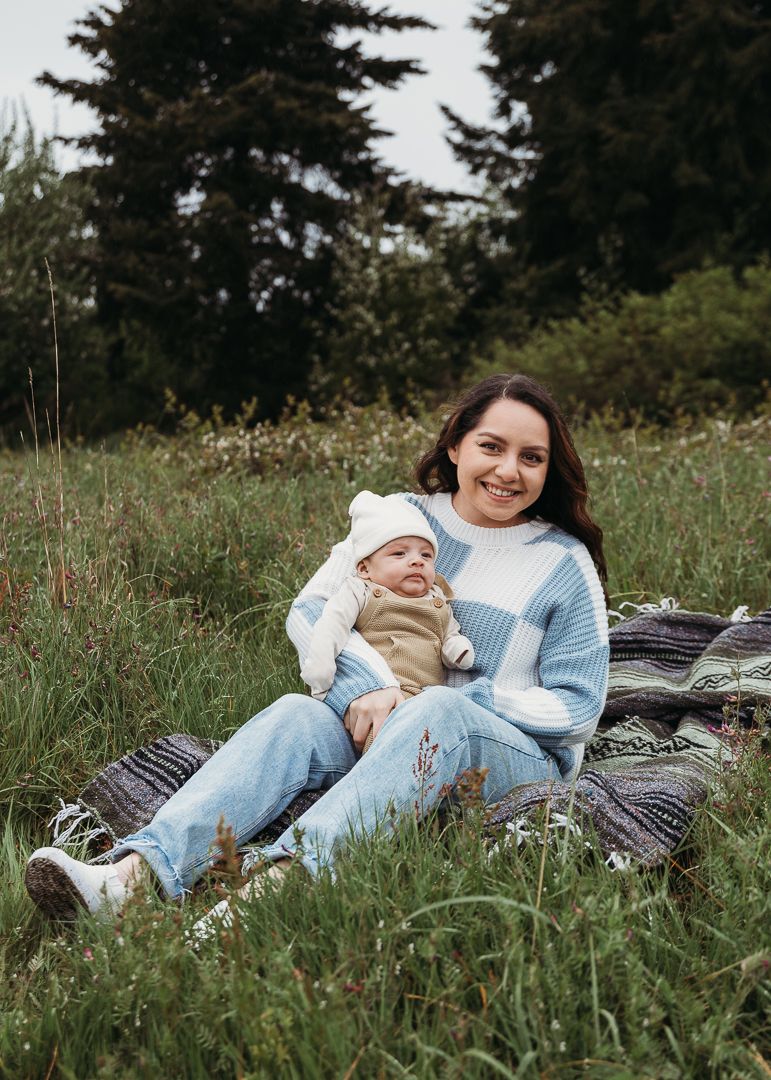 Relaxed outdoor portrait on a blanket showing tender moment between adult and baby in coordinating outfits.