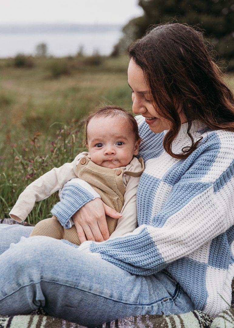 Intimate outdoor portrait showing gentle interaction between adult and infant in matching blue and white knitwear.