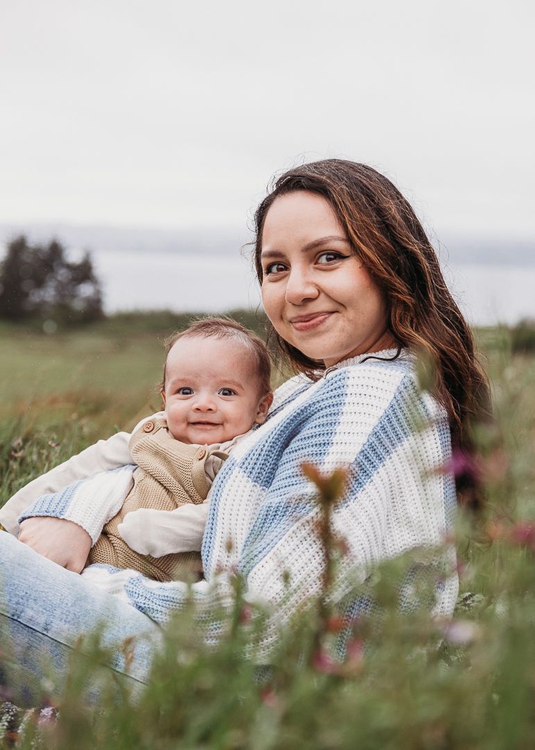 Tender moment between parent and baby sitting in a grassy meadow wearing a cozy striped sweater.