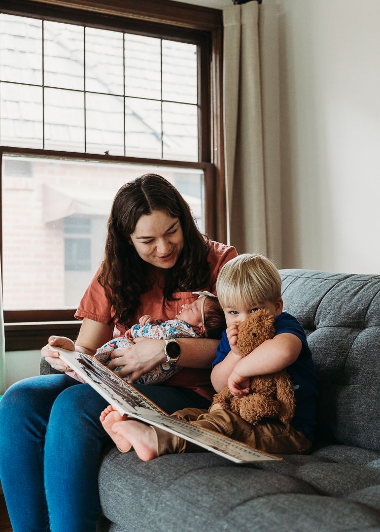 Reading time on a grey couch with a teddy bear and storybook near a window.