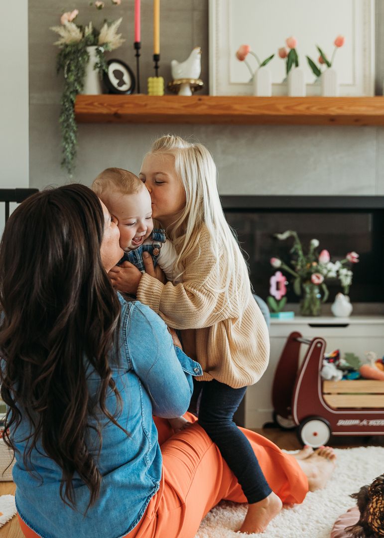 Sweet family cuddle time on a plush rug with decorative fireplace and flowers in background.