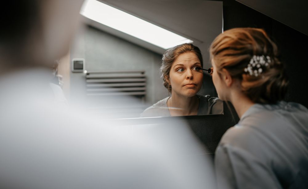 Bride with elegant updo and pearl hair accessory checking her reflection in a bathroom mirror.