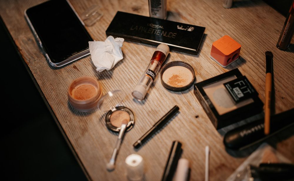 Wedding makeup products and tools scattered on a wooden table including foundation and eyeshadow.
