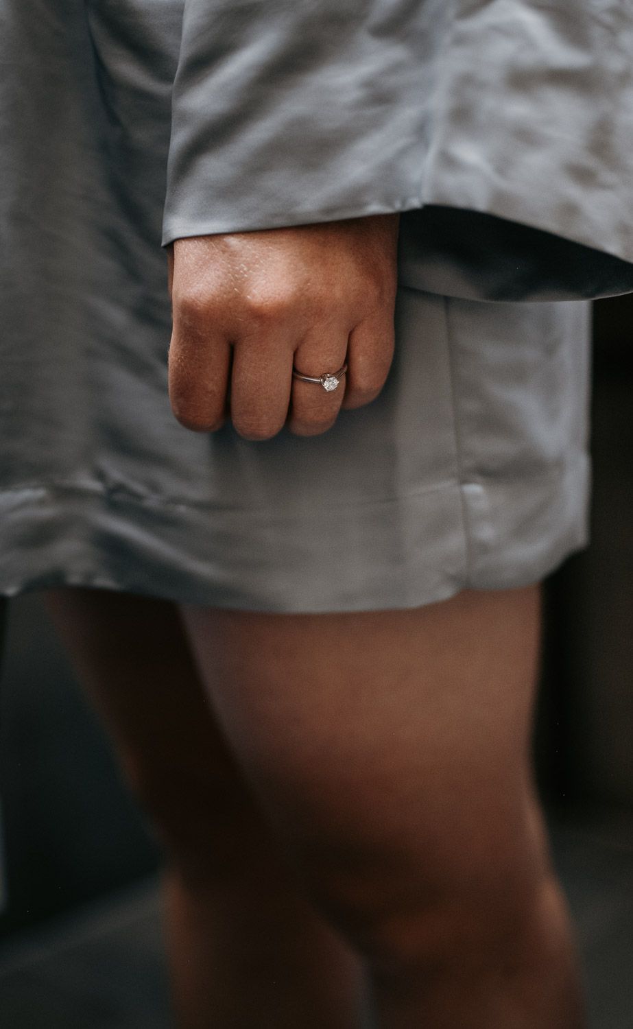 Close-up of bride in silk robe wearing a solitaire diamond engagement ring on her finger.