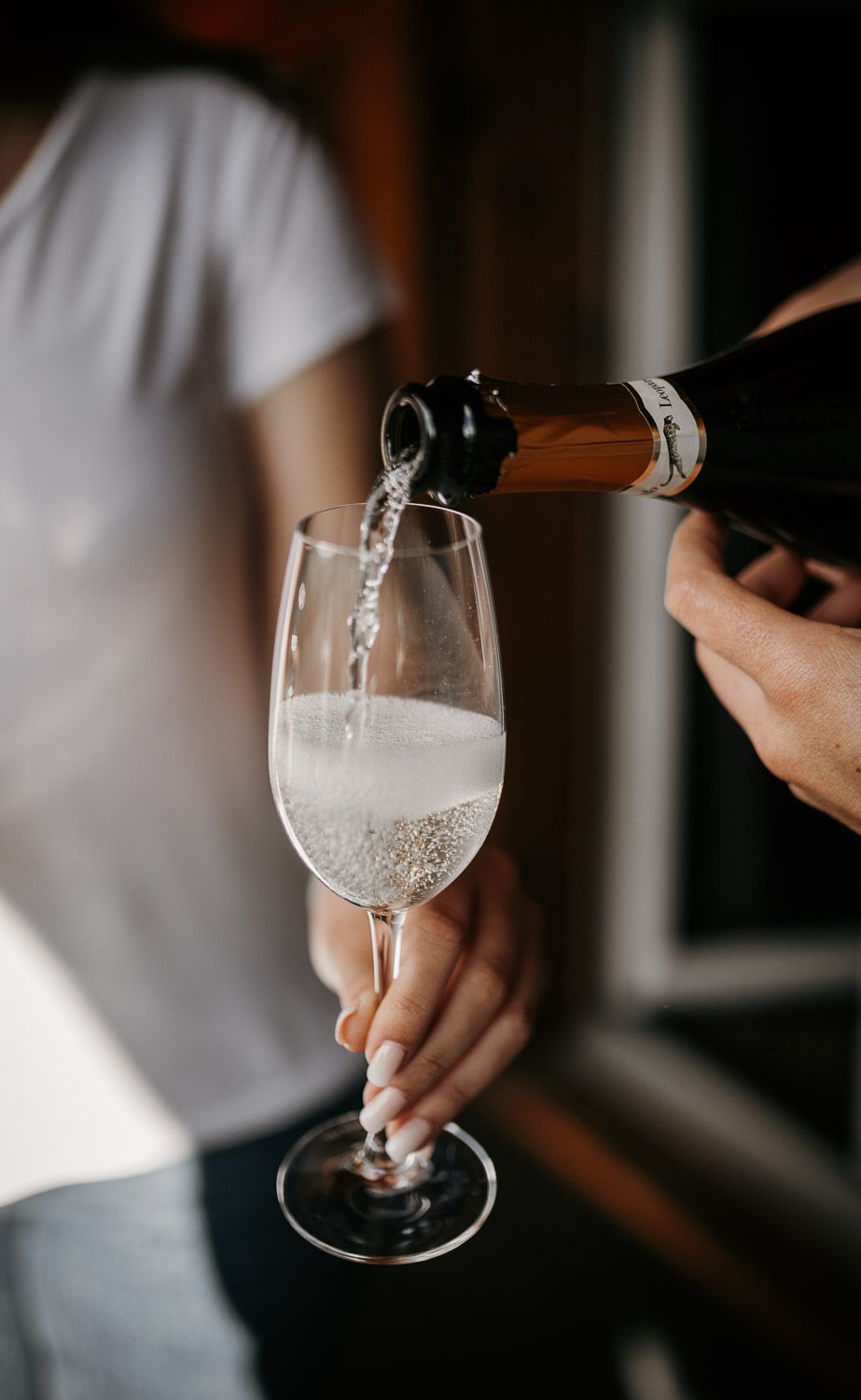 Champagne being poured into elegant flute glass held by woman in white shirt at wedding celebration.