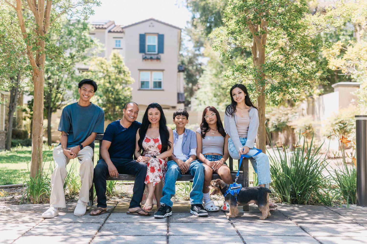 Multi-generational family sitting together on outdoor bench surrounded by greenery.