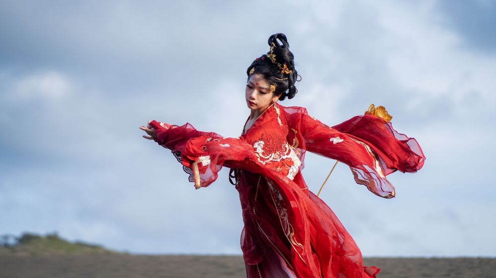 Cinematic solo portrait in flowing red Hanfu at Lake Wainamu sand dunes, evoking a fateful Desert Princess vibe, by Imagine Image Studio.