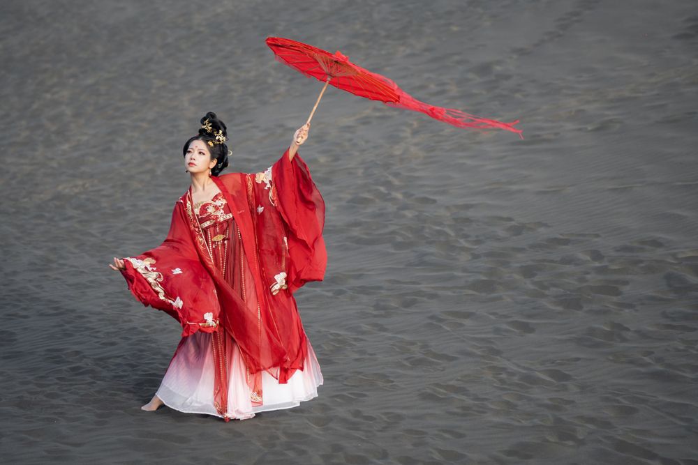 Cinematic solo portrait in flowing red Hanfu at Lake Wainamu sand dunes, evoking a fateful Desert Princess vibe, by Imagine Image Studio.