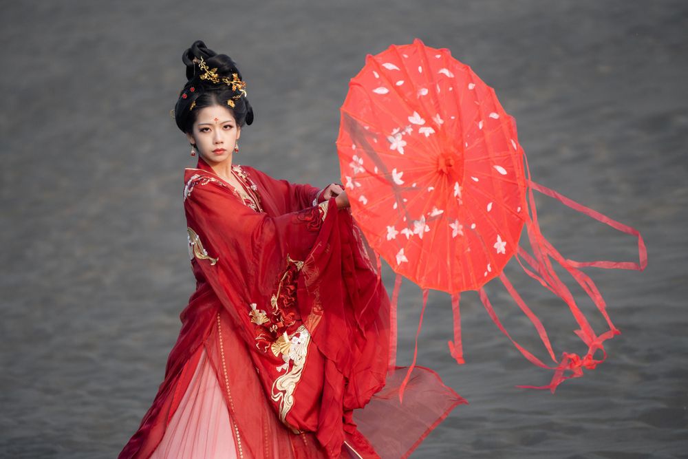Cinematic solo portrait in flowing red Hanfu at Lake Wainamu sand dunes, evoking a fateful Desert Princess vibe, by Imagine Image Studio.