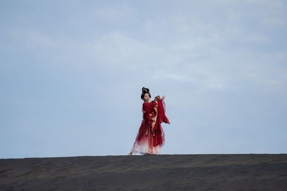 Cinematic solo portrait in flowing red Hanfu at Lake Wainamu sand dunes, evoking a fateful Desert Princess vibe, by Imagine Image Studio.