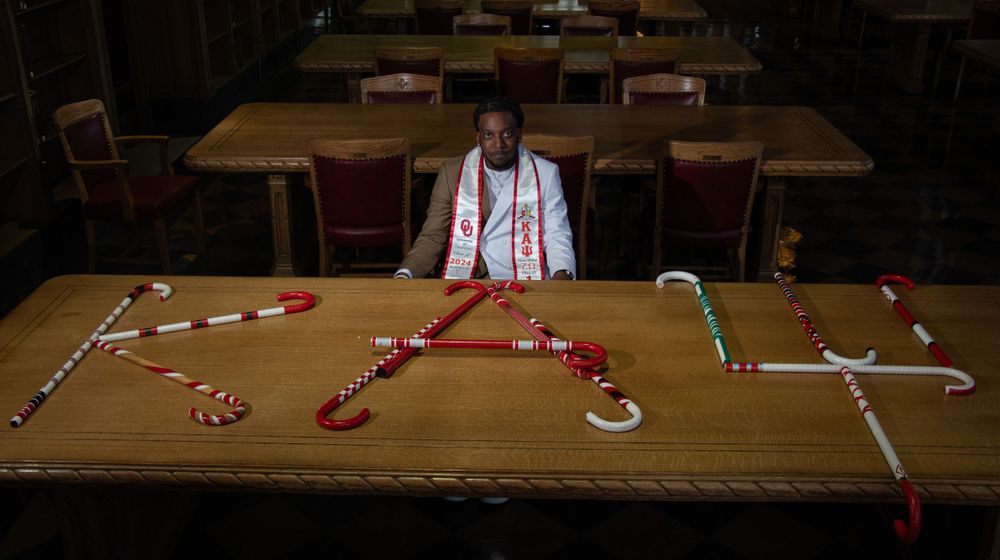 A person arranges graduation cords and stoles on a wooden table.