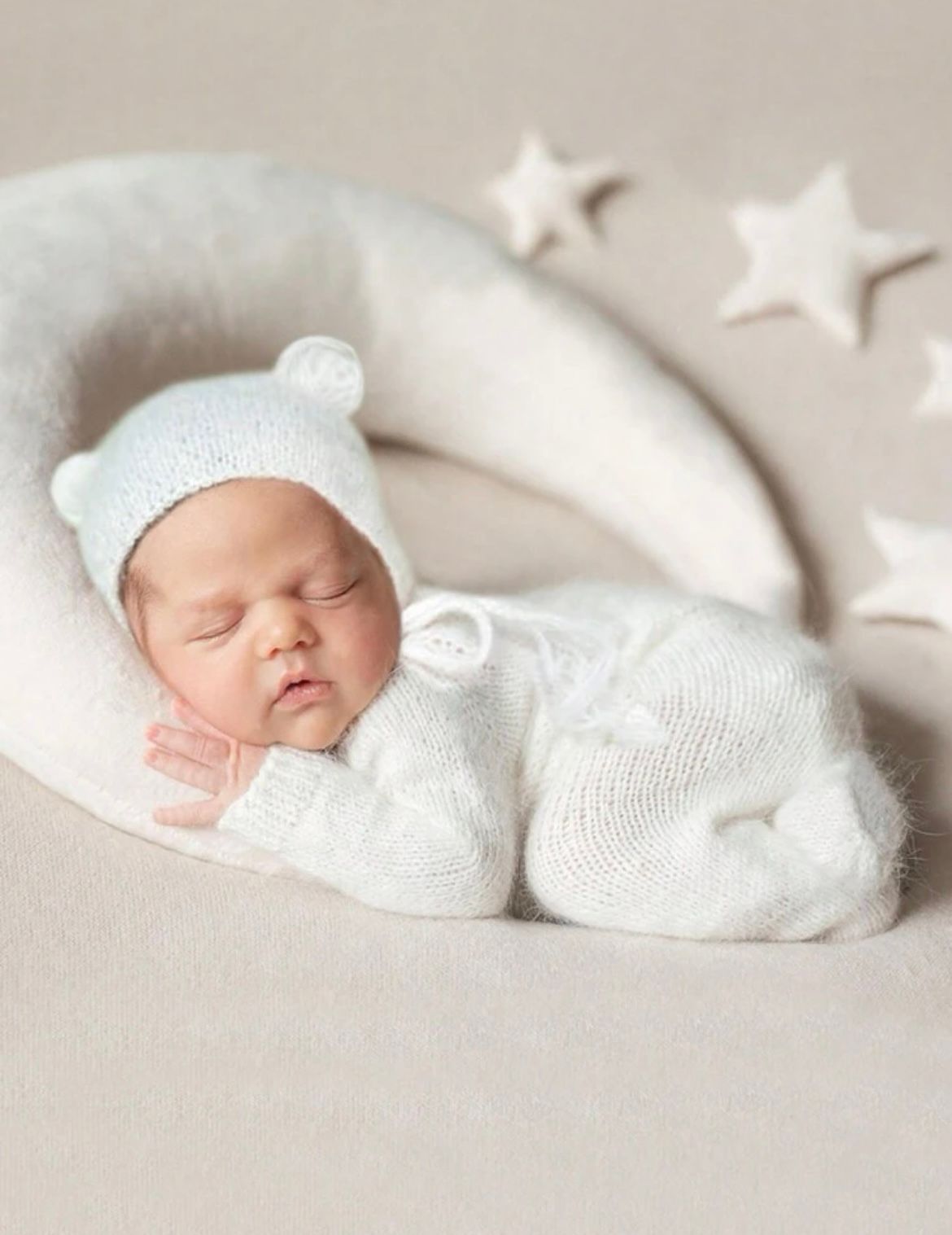 Peaceful newborn baby sleeping in white knit outfit with star decorations.