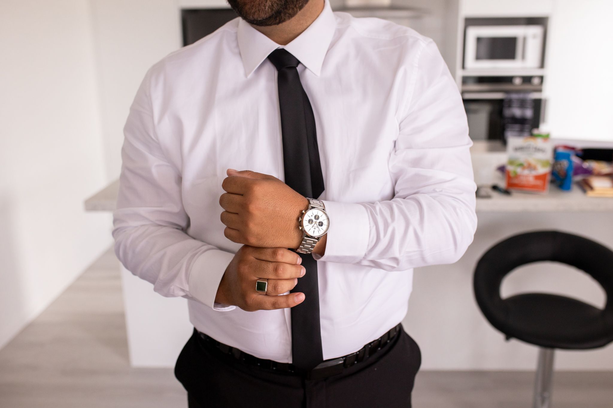 Close-up of a person adjusting their tie and cufflinks while wearing a crisp white dress shirt.