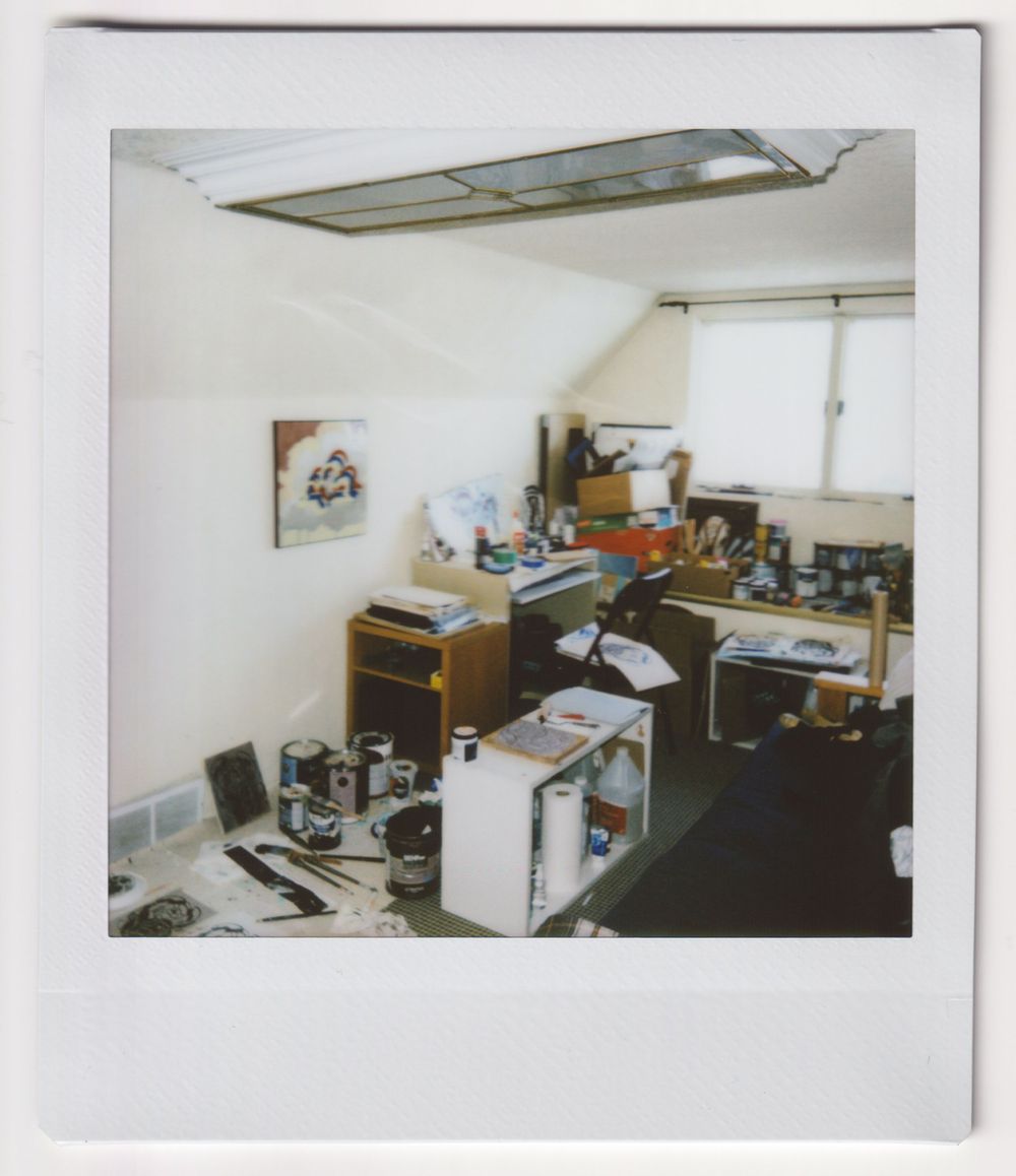 Cluttered office space with computer equipment, desk, and overhead fluorescent lighting.