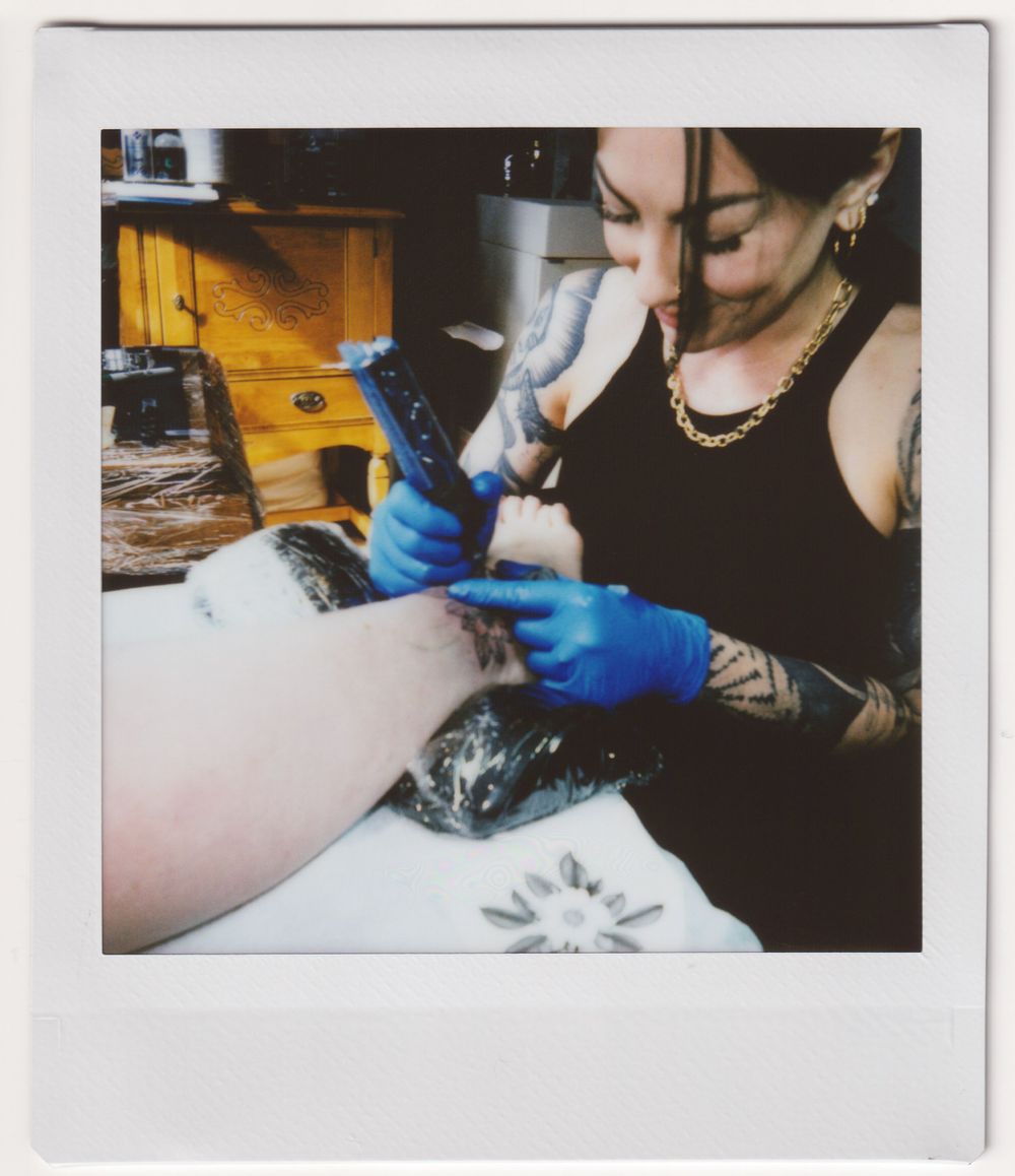 Close-up of tattooing process showing gloved hands working with tattoo machine.
