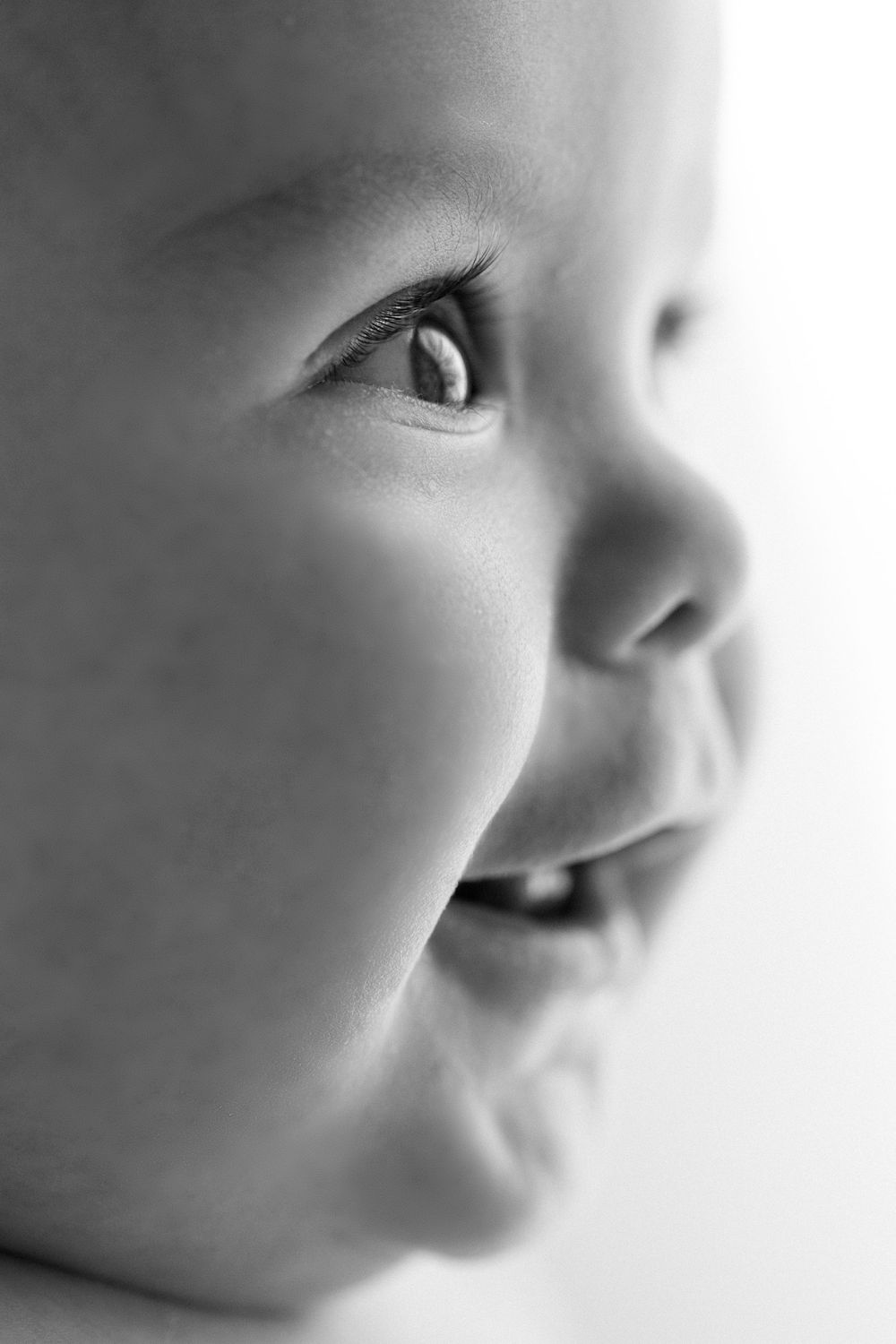 A close-up black and white portrait showing the side profile of a small child with soft features and a gentle smile.