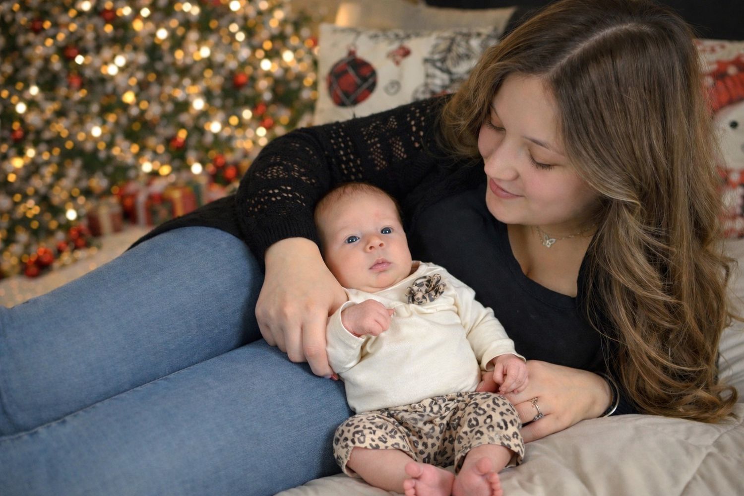 A parent and baby share a tender moment on the couch in front of a decorated Christmas tree.